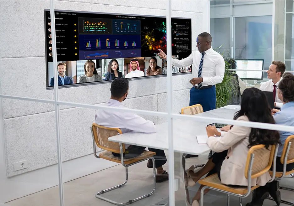 Team using a JAV H15 interactive display for a presentation in a hybrid meeting, with one person standing and pointing at data and video participants on screen.