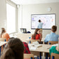 Presenter annotating data charts on a large JAV smart board during an interactive classroom lesson with students.