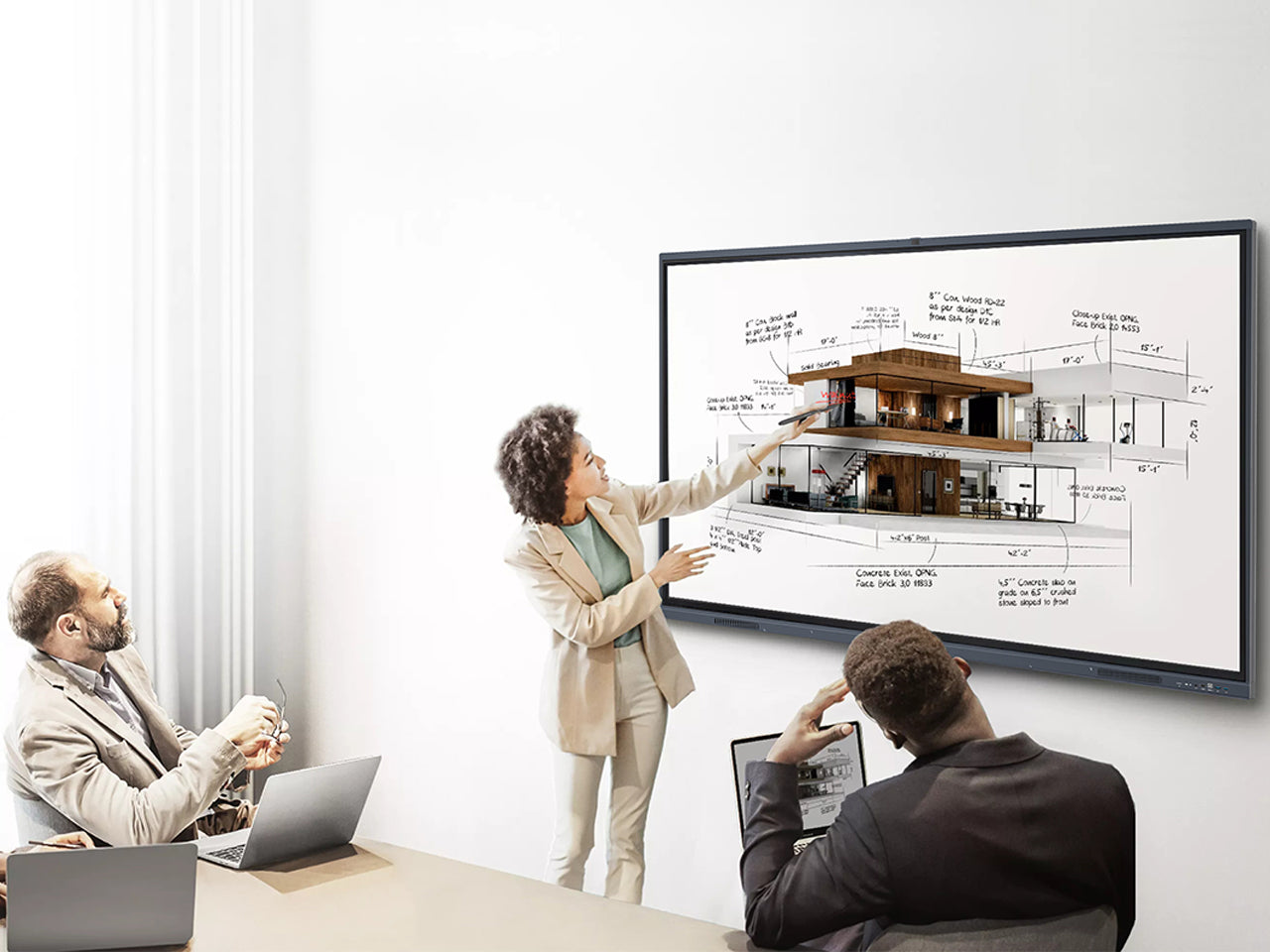 Presenter annotating an architectural drawing on a large JAV interactive display during a design review meeting with colleagues.